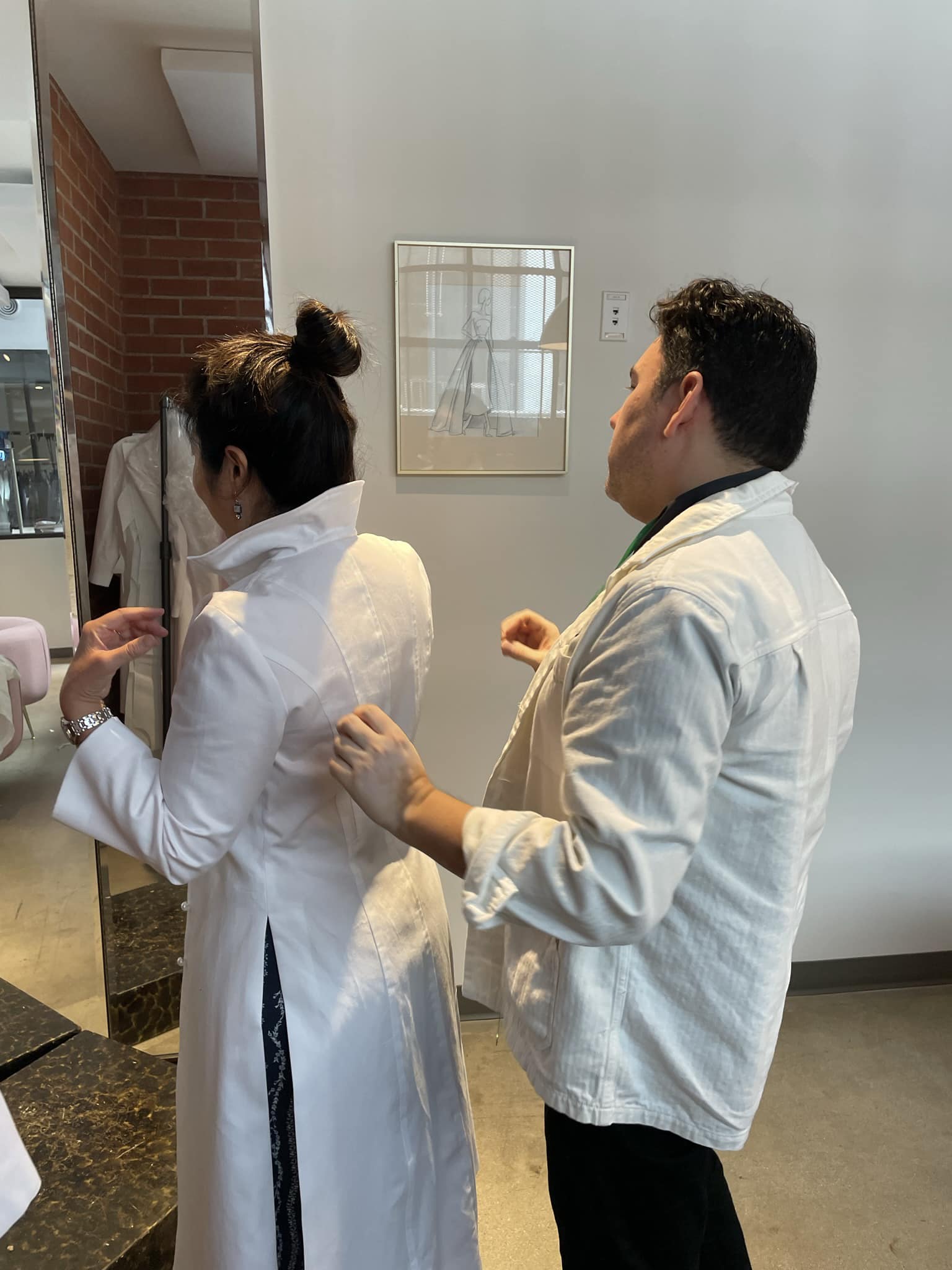 Person adjusting another's white coat in store.